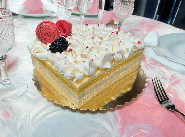 A slice of French Exotic cake, featuring layers of light sponge cake, tropical fruit filling, and a delicate whipped cream topping.