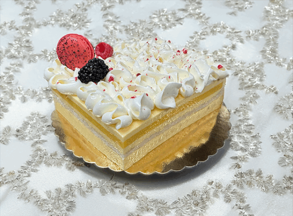 A slice of French Exotic cake, featuring layers of light sponge cake, tropical fruit filling, and a delicate whipped cream topping.